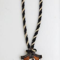Shield-like shaped medal with magpie and black, white and brown enamel. Black, white twined cord. Silver text.