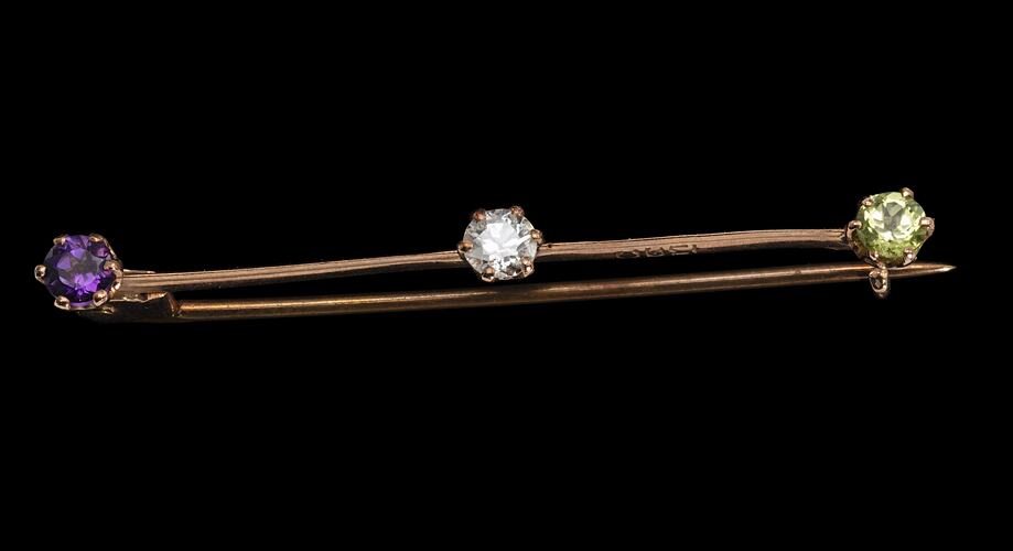 Rose gold bar brooch with three paste stones. Purple at left end, white in centre and light green at right end.