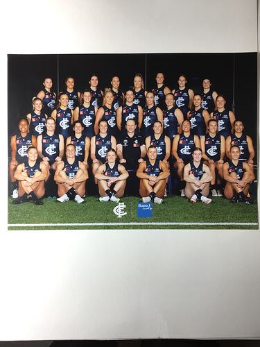 Group portrait of female footballers wearing blue jumpers with white logo.