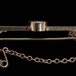 Profile of gold bar brooch with central oval opal. Fine saftey chain attached at left.