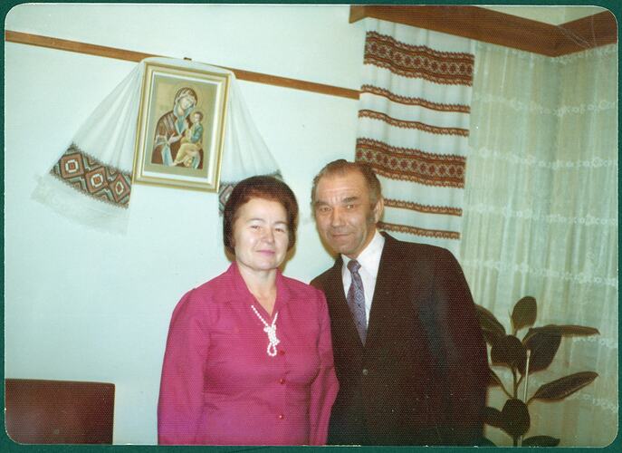 Woman and man posing in front of a Ukrainian icon with handwoven and embroidered traditional wall hanging draped over the icon. There is also a handwoven and embroidered window drape behind them.