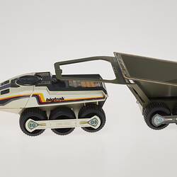 Cream six-wheeled toy truck with grey two-wheeled trailer. Stickers on sides. Left profile.