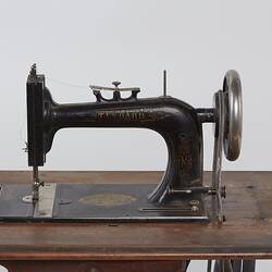 Detail of sewing machine fitted to a metal frame with a wooden bench.