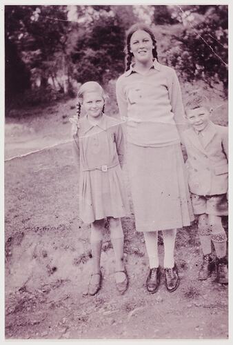 Tall girl stands in centre with girl to the left and boy to the right.
