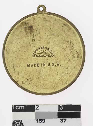 Round gold coloured medal with text in centre.