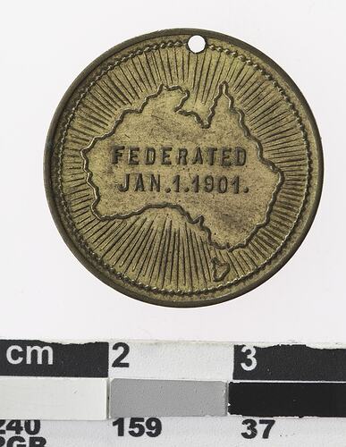 Round gold coloured medal with map of Australia with lines radiating and text in centre.