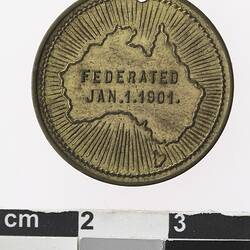Round gold coloured medal with map of Australia with lines radiating and text in centre.