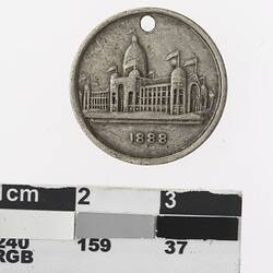 Round silver coloured medal with building and text below.