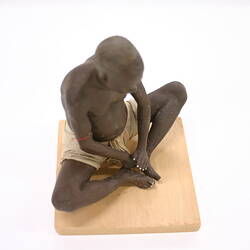 Figure of an Indian man, seated with knees wide.