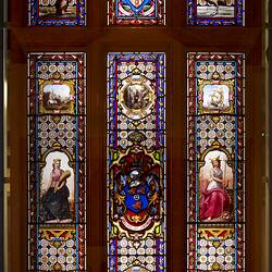 Stained glass window. Three longer vertical panels, each with a smaller section above.