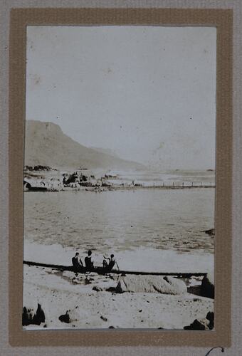 Three men sitting on shore of beach,