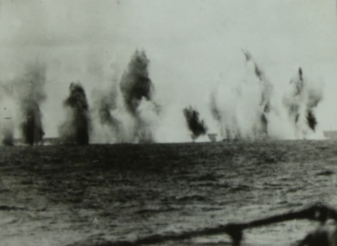 Multiple explosions in the water in background, ocean in is the foreground.