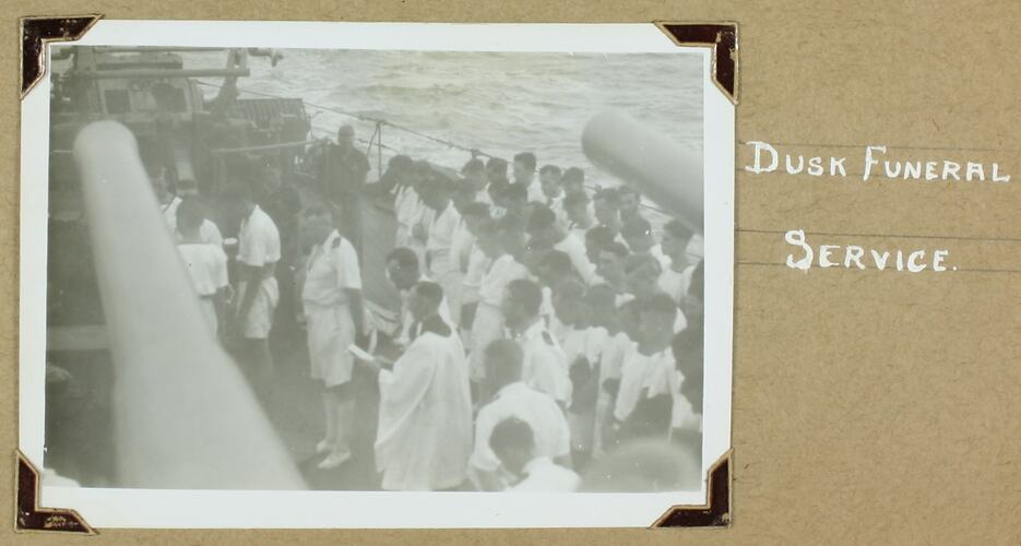 Large group of uniformed sailors with their heads bowed Standing on the deck of a ship.