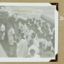 Large group of uniformed sailors with their heads bowed Standing on the deck of a ship.