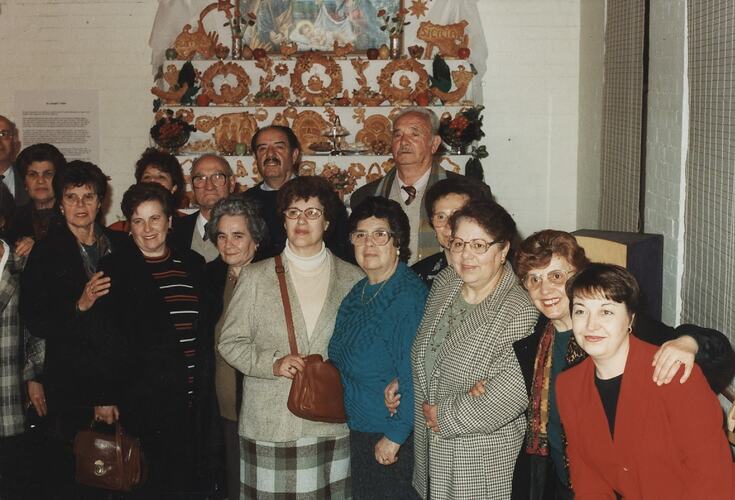 Group posing in front of multi-tiered table covered in decorative votive breads. Religious painting at back ce