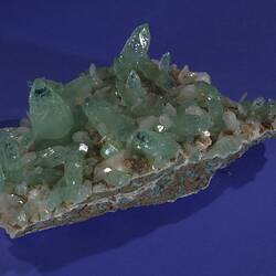 Pale green and white crystals on a grey rock with turquoise patches.