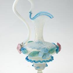 Blue blown-glass ewer, spiral fluted neck, serpentine handle, flattened bulbous body layered with pink, blue, green flowers and leaves.