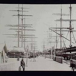 Freight being unloaded from a number of sailing ships moored at a pier.
