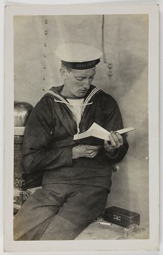 Man in Navy uniform seated reading a book.