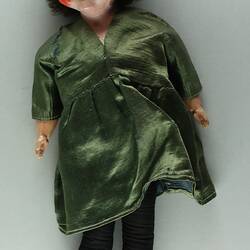 Female doll, porcelain head with short brown hair. Soft body. Wearing olive green satin dress.