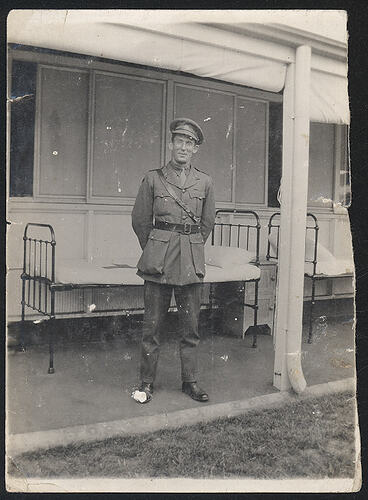 Serviceman on a veranda standing in front of two hospital beds.