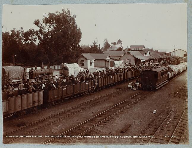 Trains at a railway station with open carriages carrying large group of men.
