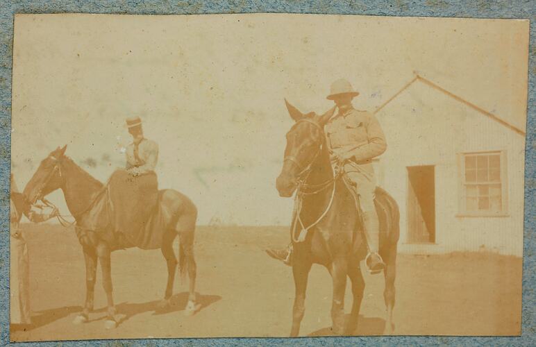 Man and woman riding horses with building in background.