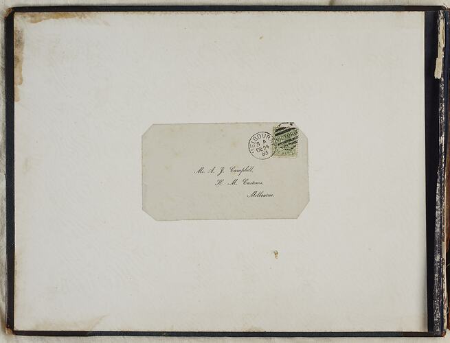 Inside book cover with affixed white sheet and label. Label has printed cursive text. Stamp and postage stamp