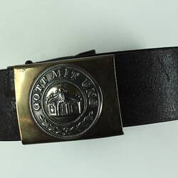 Leather belt with buckle featuring a crown and inscription, belt rolled into circle.