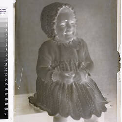 Negative, female toddler in knitter dress and bonnet.