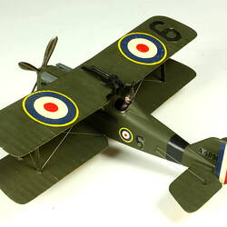 Dark green model airplane. Circle pattern on top on each wing. Rear left view.