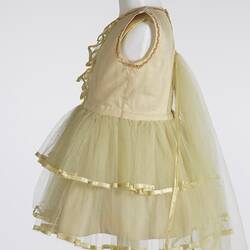 Back of yellow child's dress, sleeveless, layered lace skirt, gold trim. Left profile.