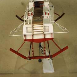 Back view of white metal hydrofoil model with red hull and skis. White deck.