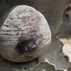Grey cannnon ball shaped rock embedded in rockface.