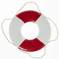 Red and white miniature lifebuoy. Rope around rim. Back view.