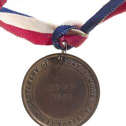 Round copper medal with date in centre. Text around. Suspended from red, white and blue ribbon.