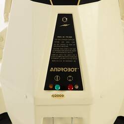 Detail of label on cream plastic robot with angular human-like shape, ie. head, shoulders, waist and legs. Black plastic features.