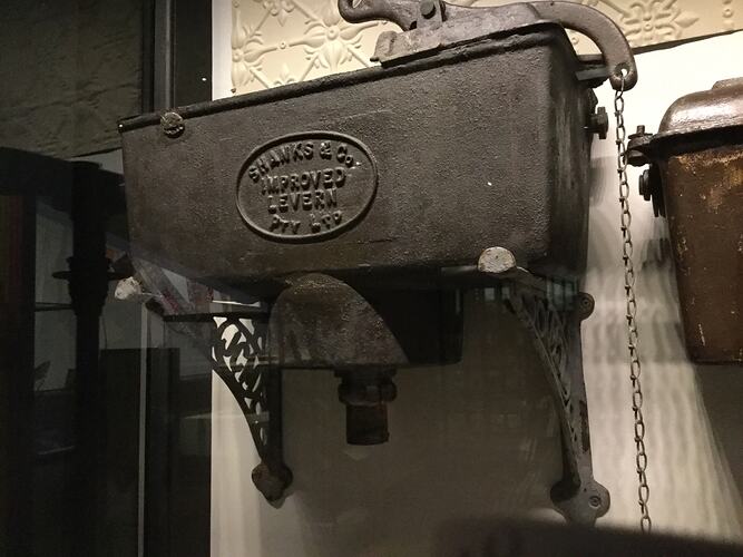 Black cast irn rectangular cistern with raised lettering in centre. Pull chain at right.