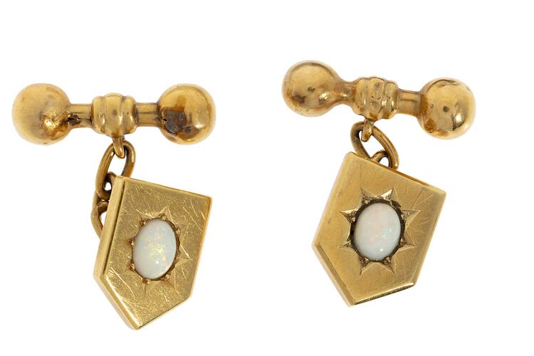 Gold cufflinks of heraldic shield design with centrally placed opals, chains to bar-bells.