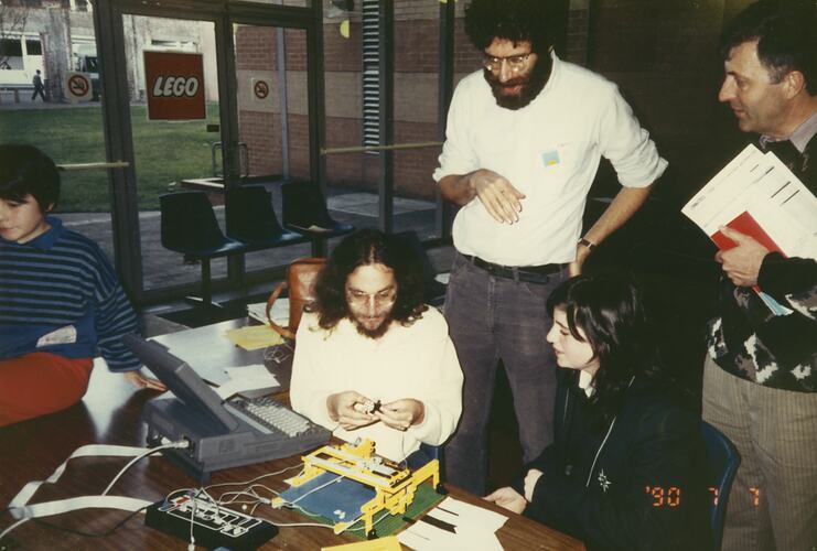 A group of men and women surrounding a laptop and Lego construction.