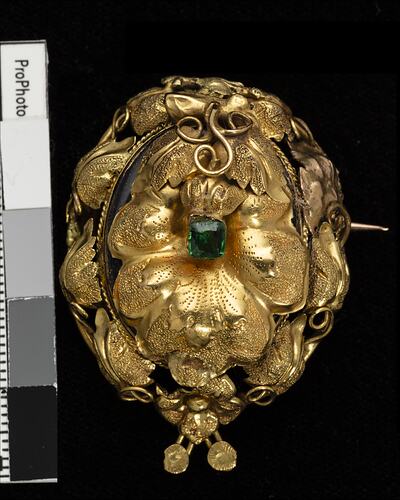 Round gold brooch with leaves and tendrils. Green paste stone in centre.