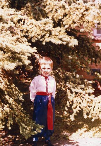 Young boy standing in front of tree wearing traditional Ukrainian clothing.