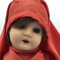 The face of a doll dressed in a red gown and long head scarf