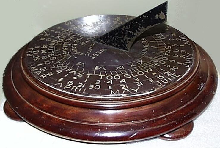 Round wooden disc on low feet with round slate sundial top and iron gnomon.