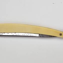 Cut throat razor, metal blade, ivory-styled plastic handle. Closed.