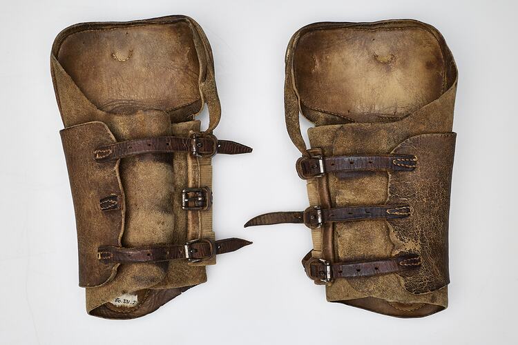 Tan coloured leather shin pads fastened with three dark brown leather straps and buckles.
