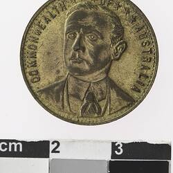 Round gold coloured medal with profile of man and text surrounding,