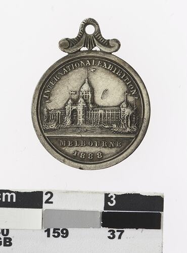 Round silver coloured medal with building, text above and below.