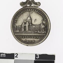 Round silver coloured medal with building, text above and below.