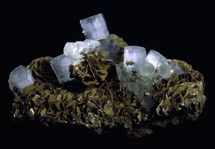 Pale crystal columns on a base of platy brown mineral.